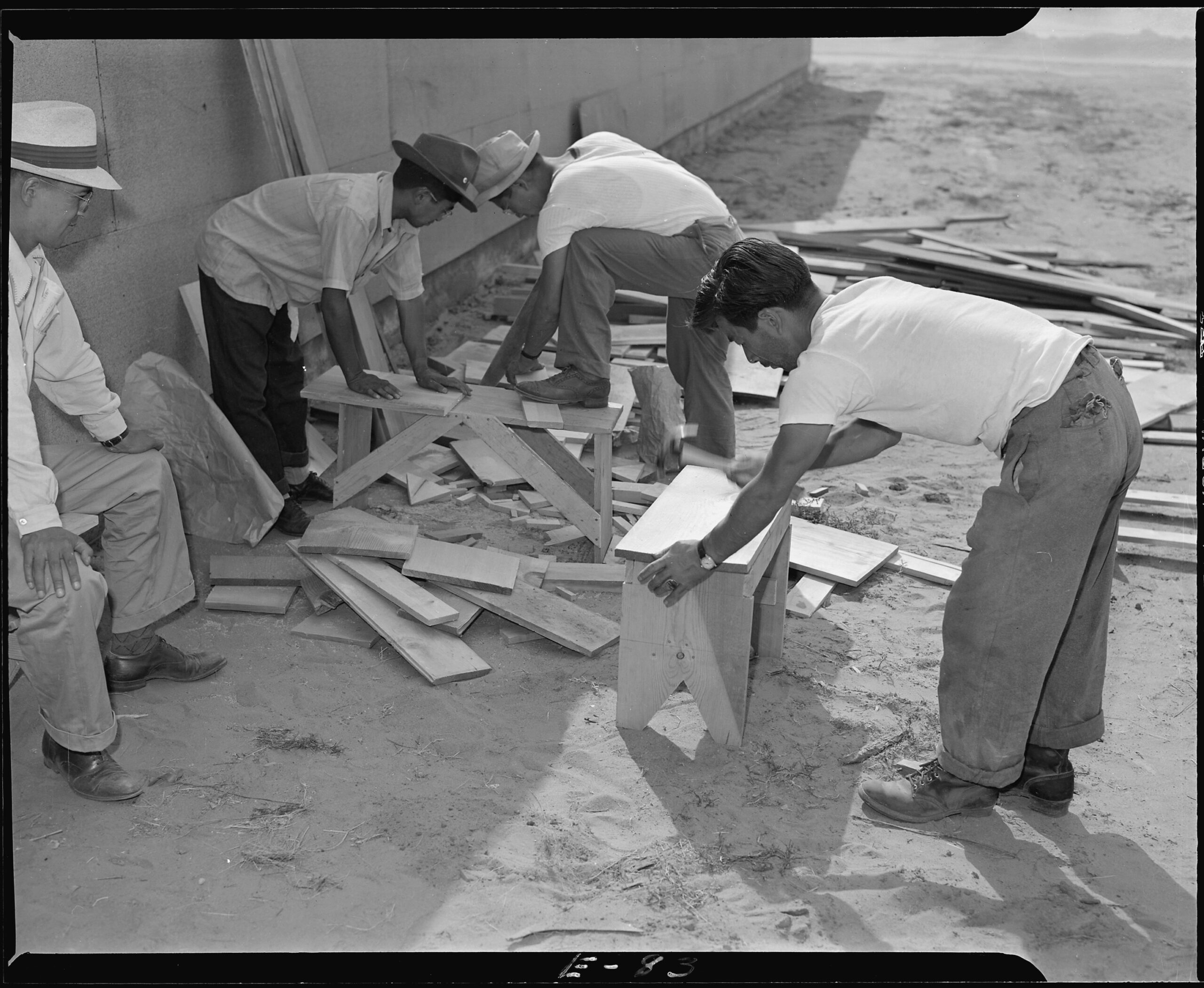 Early arrivals preparing benches and make shift seats to provide temporary furniture in their barracks. Photographer: Parker, Tom; Amache, Colorado. Courtesy of UC Berkeley, Bancroft Library